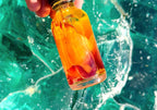 A hand holding a bottle of Mokupuni with rose petals inside against a glass rock background
